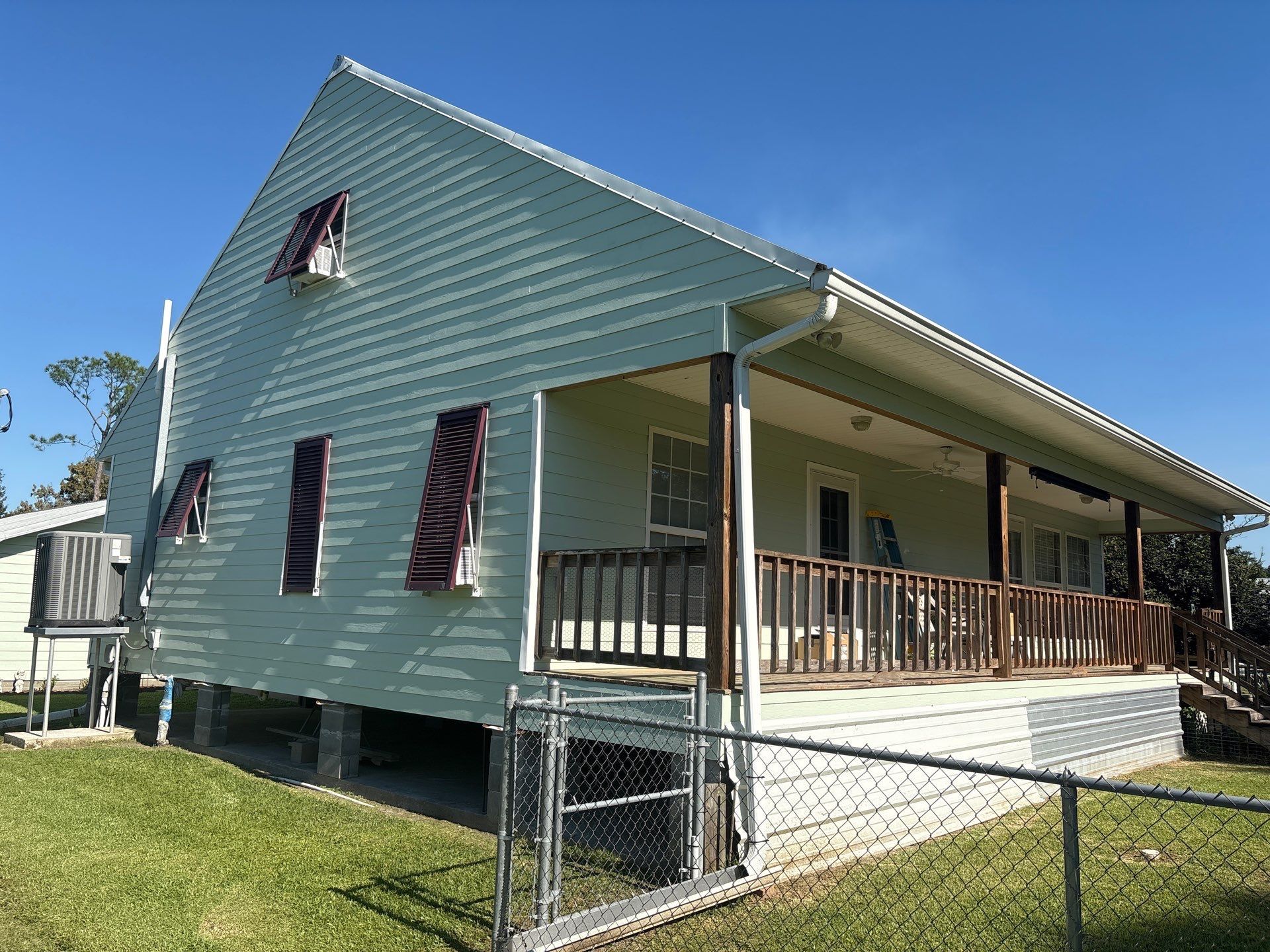 Light green house with a porch and red shutters, under a blue sky.