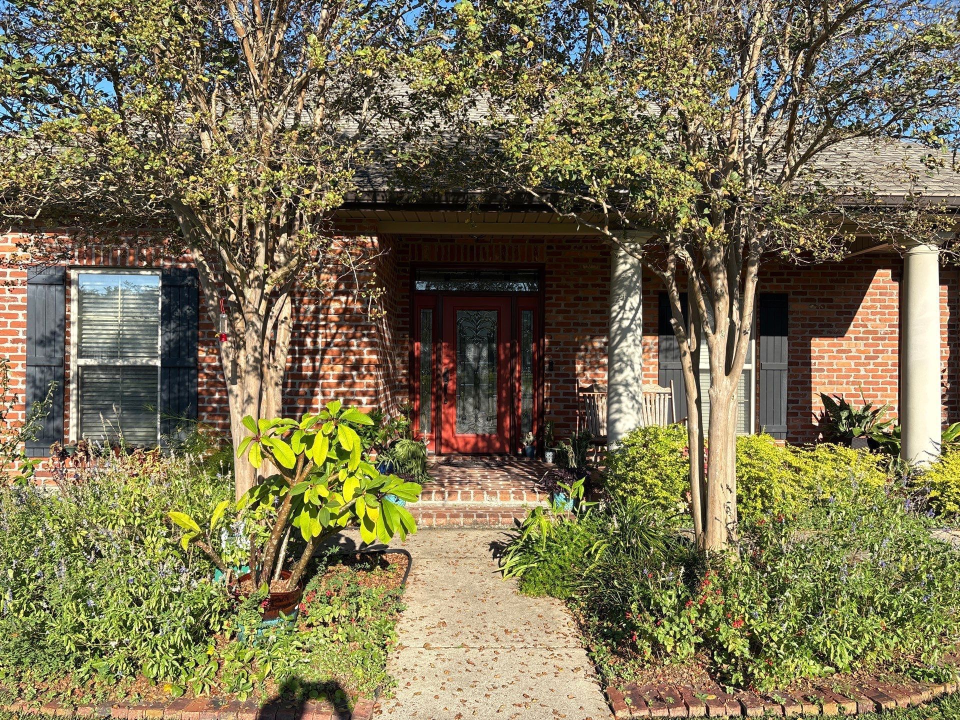 Red brick house with a front porch, flanked by trees and greenery.