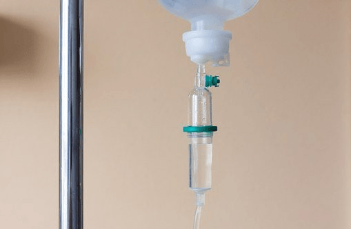 IV drip bag and tubing hanging from a metal pole against a beige wall