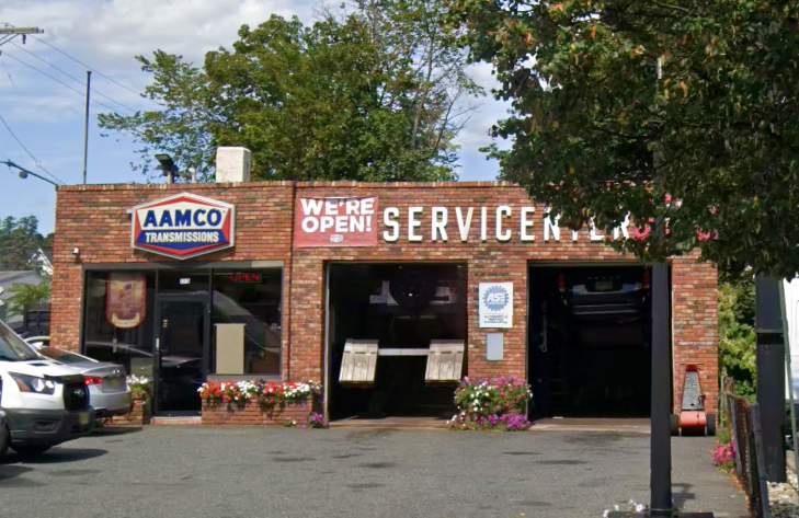 An aerial view of an AAMCO Transmissions & Total Car Care shop with multiple bays, adjacent to a residential area on a sunny day.