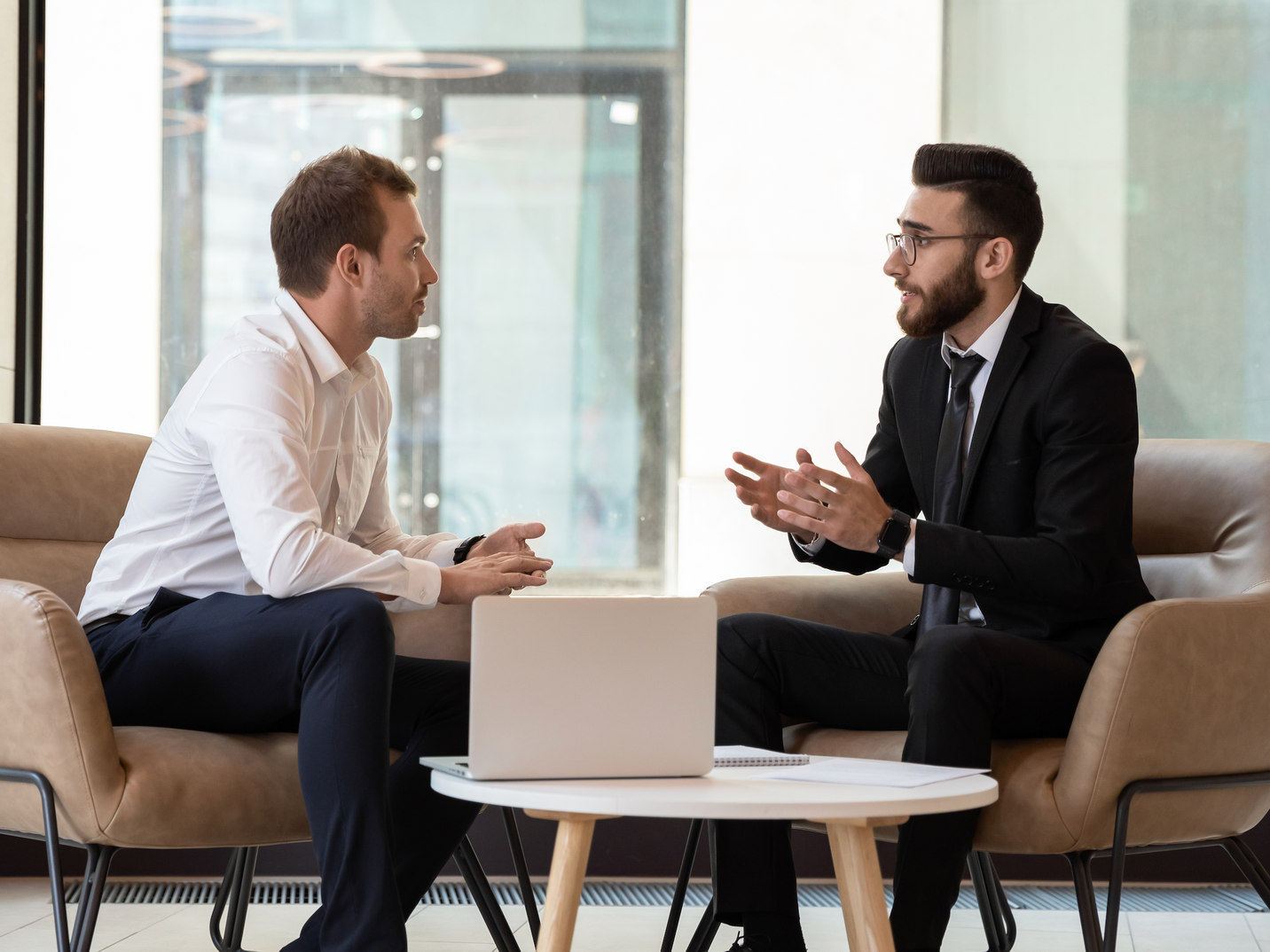 Two men are sitting at a table talking to each other.