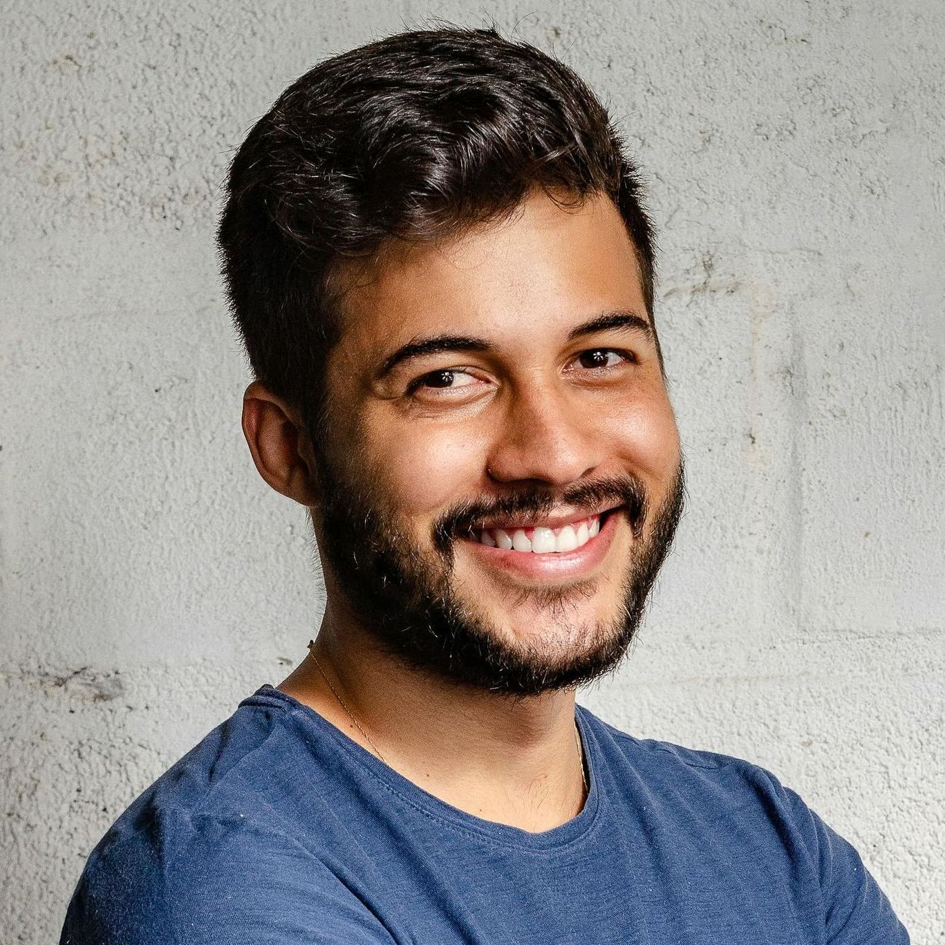A man with a beard is smiling and wearing a blue shirt.