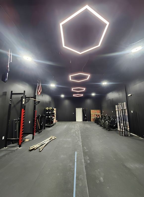 Long gym interior with hexagon ceiling lights, racks and equipment along the walls, and a central walkway