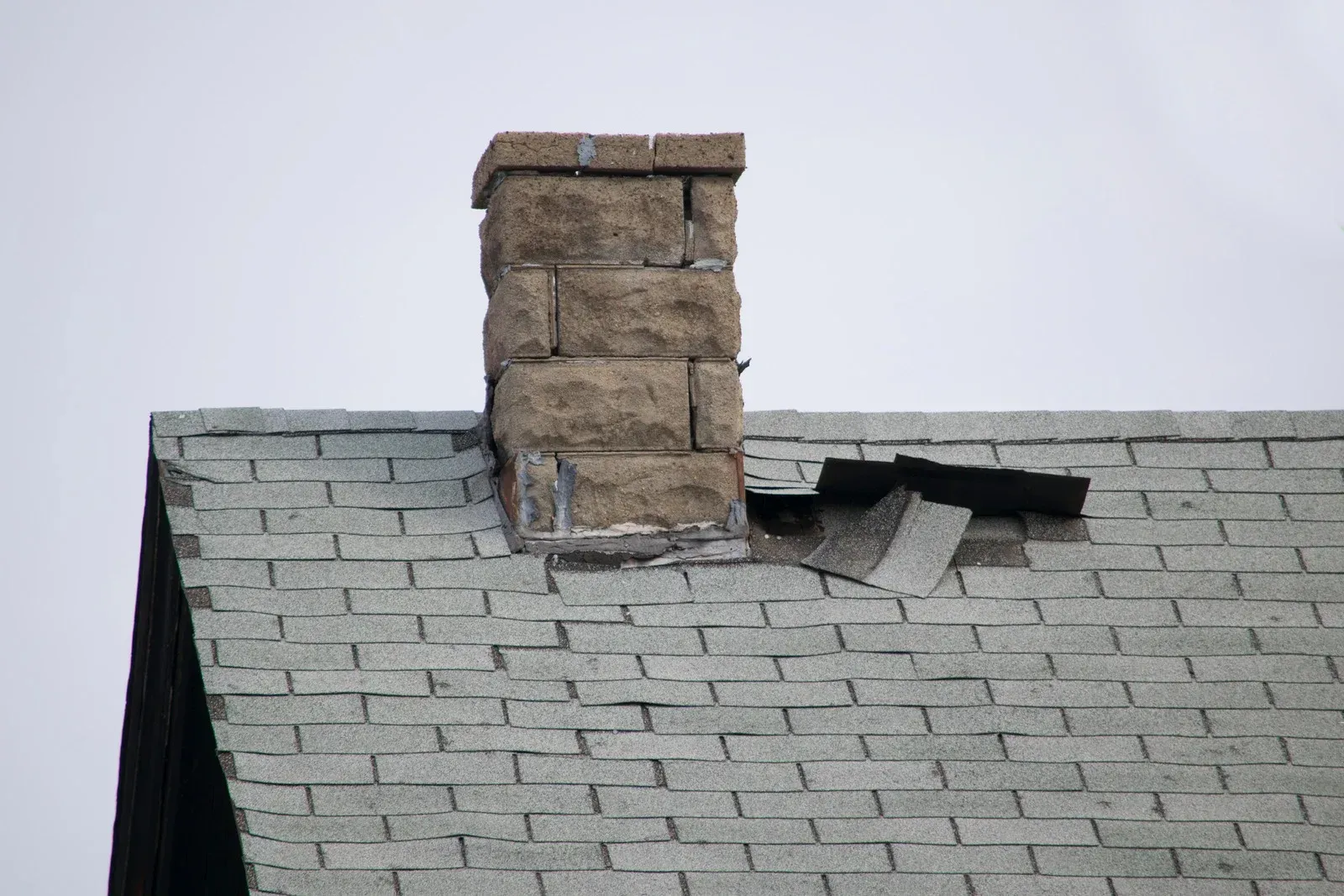 Damaged roof with a brick chimney and a hole in the shingles