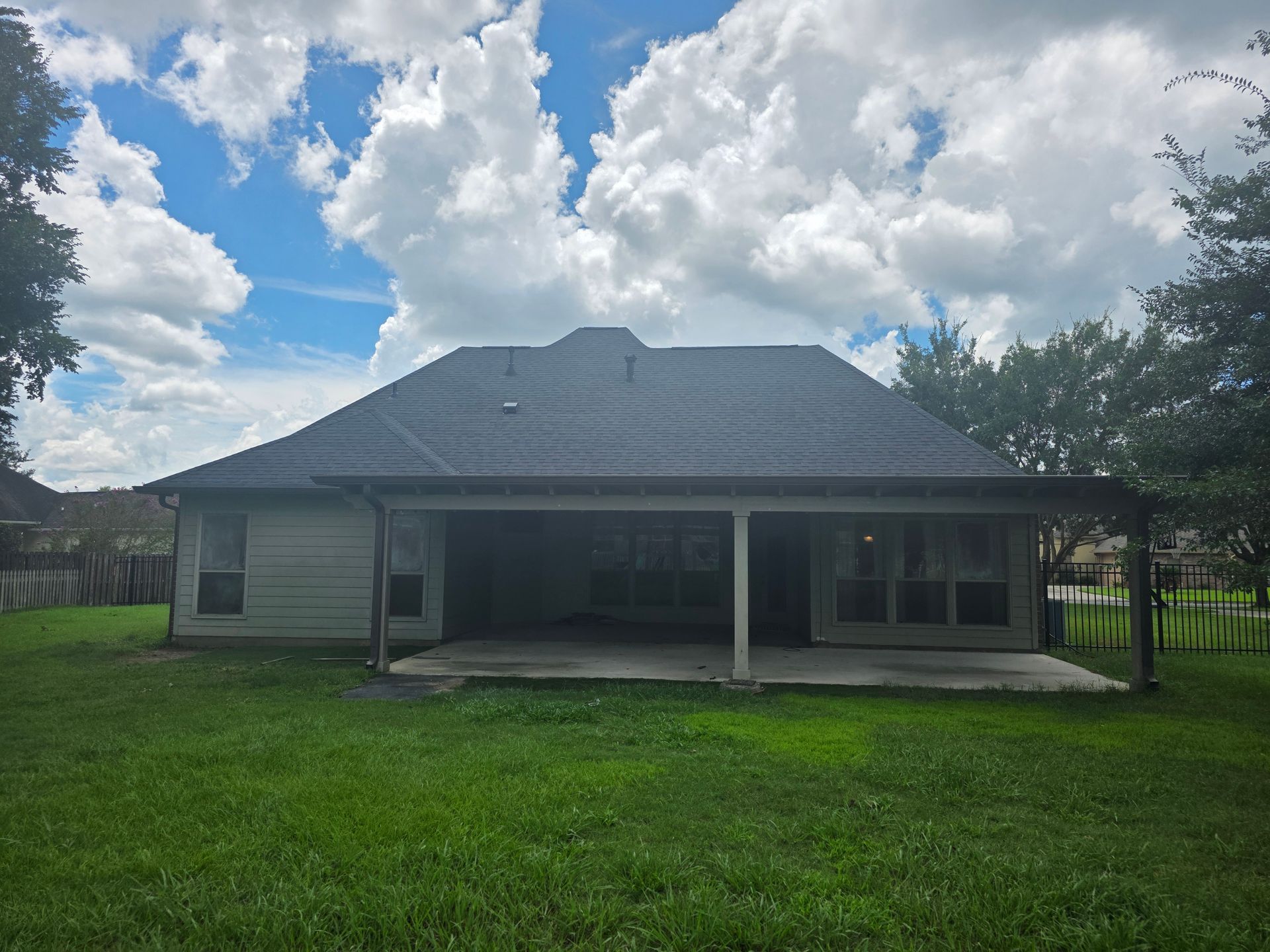 Single-story house with a covered porch and large green lawn under a cloudy sky