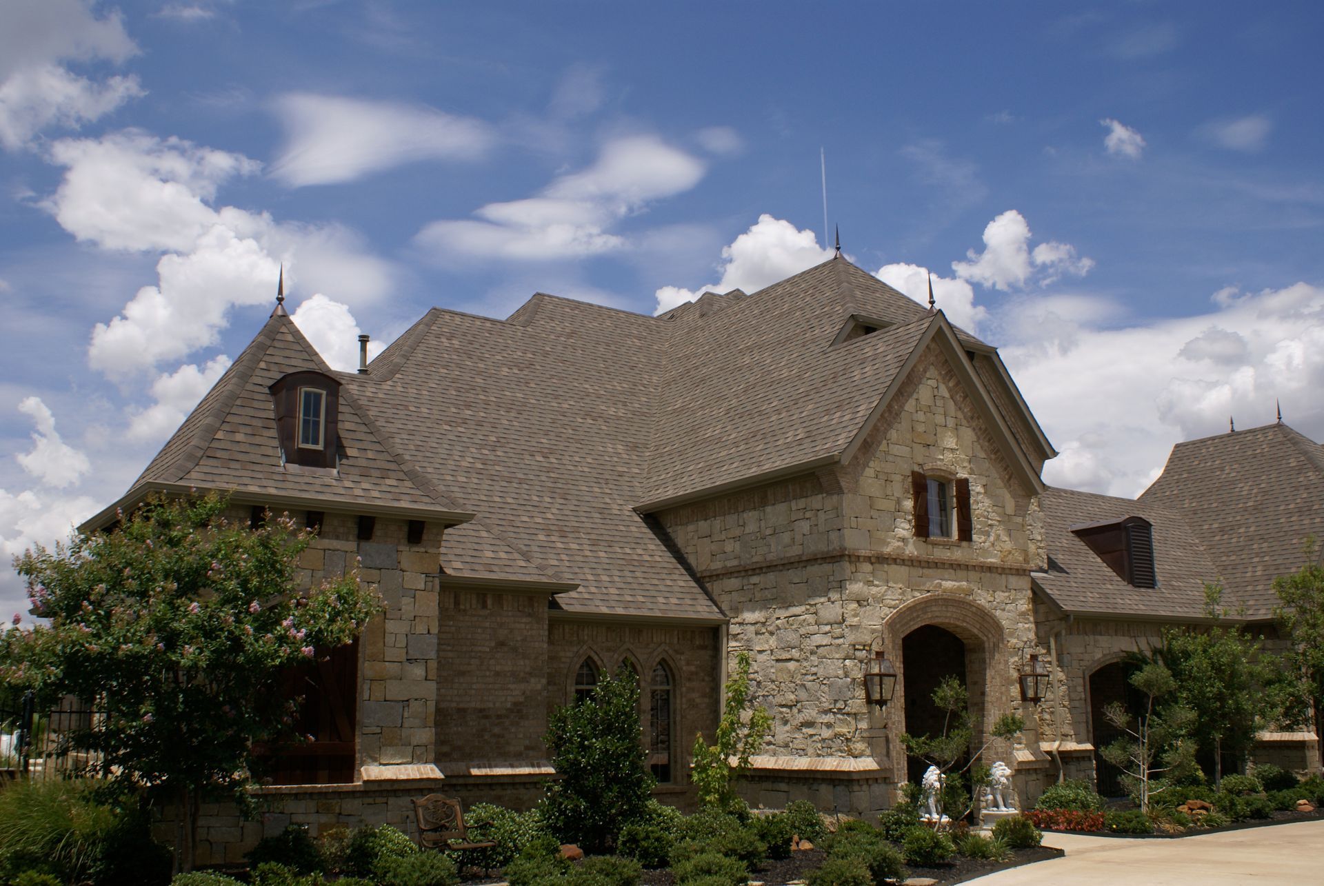 Stone house with steep roof and arched entryway under a blue sky with clouds