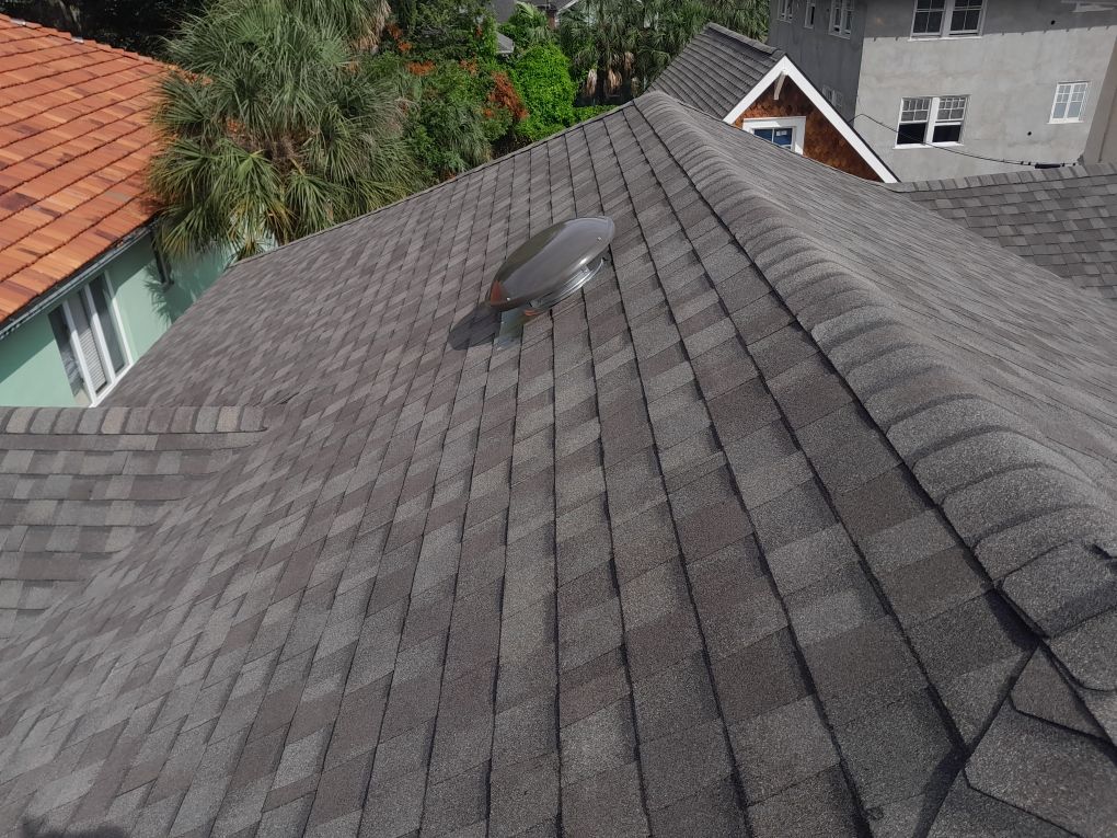 Gray shingled roof with a small skylight, viewed from above near neighboring houses and trees
