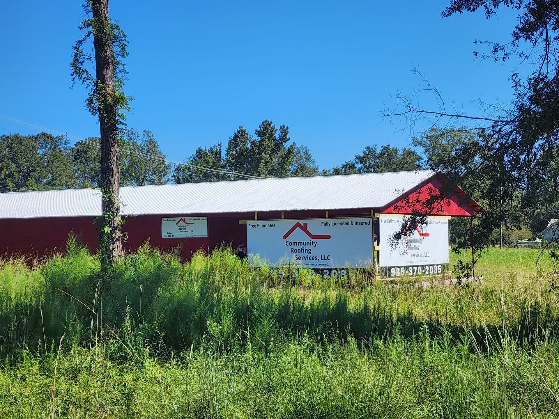 Red building with white roof and signs, partly hidden by tall grass and trees under a blue sky