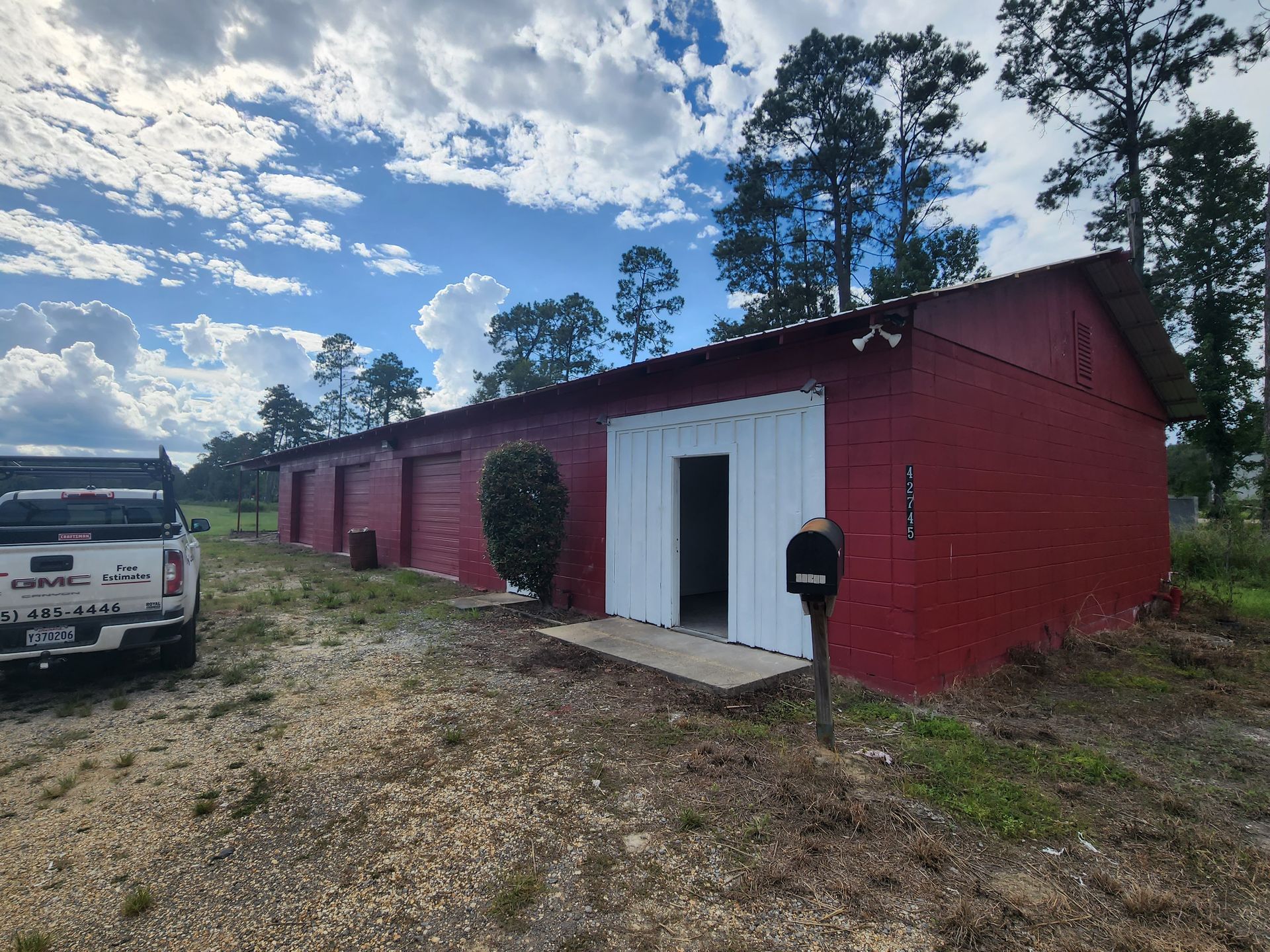 Red metal building with white double doors and a black mailbox, next to a white truck under a cloudy sky.