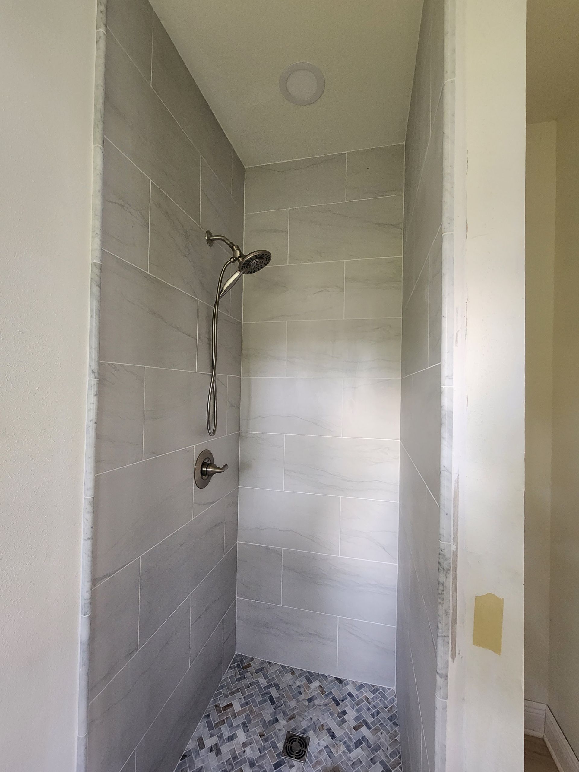Narrow tiled shower stall with chrome showerhead, grab bar, and pebble-style shower floor.