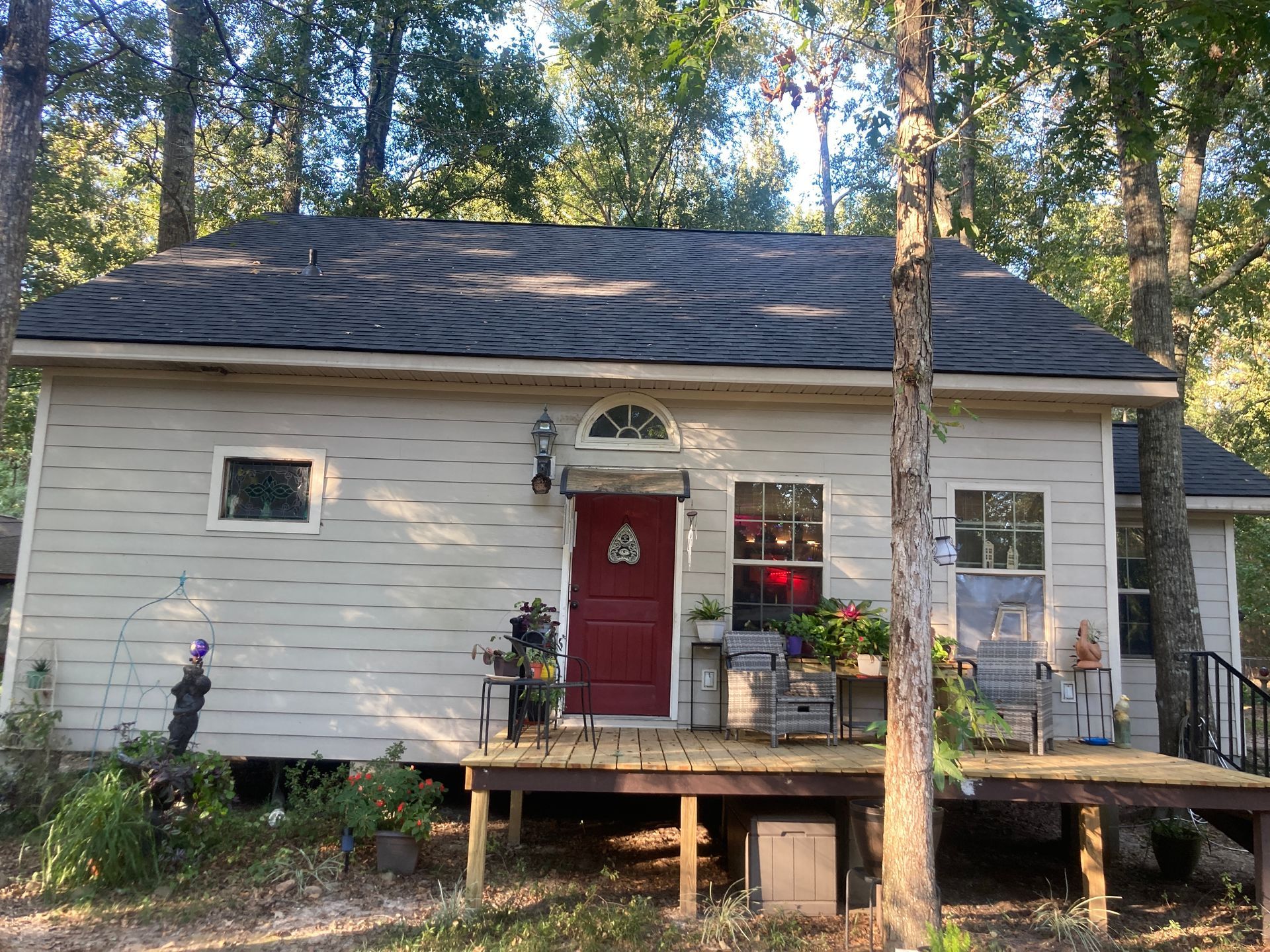 Small white house with red door, front porch, and trees in the background