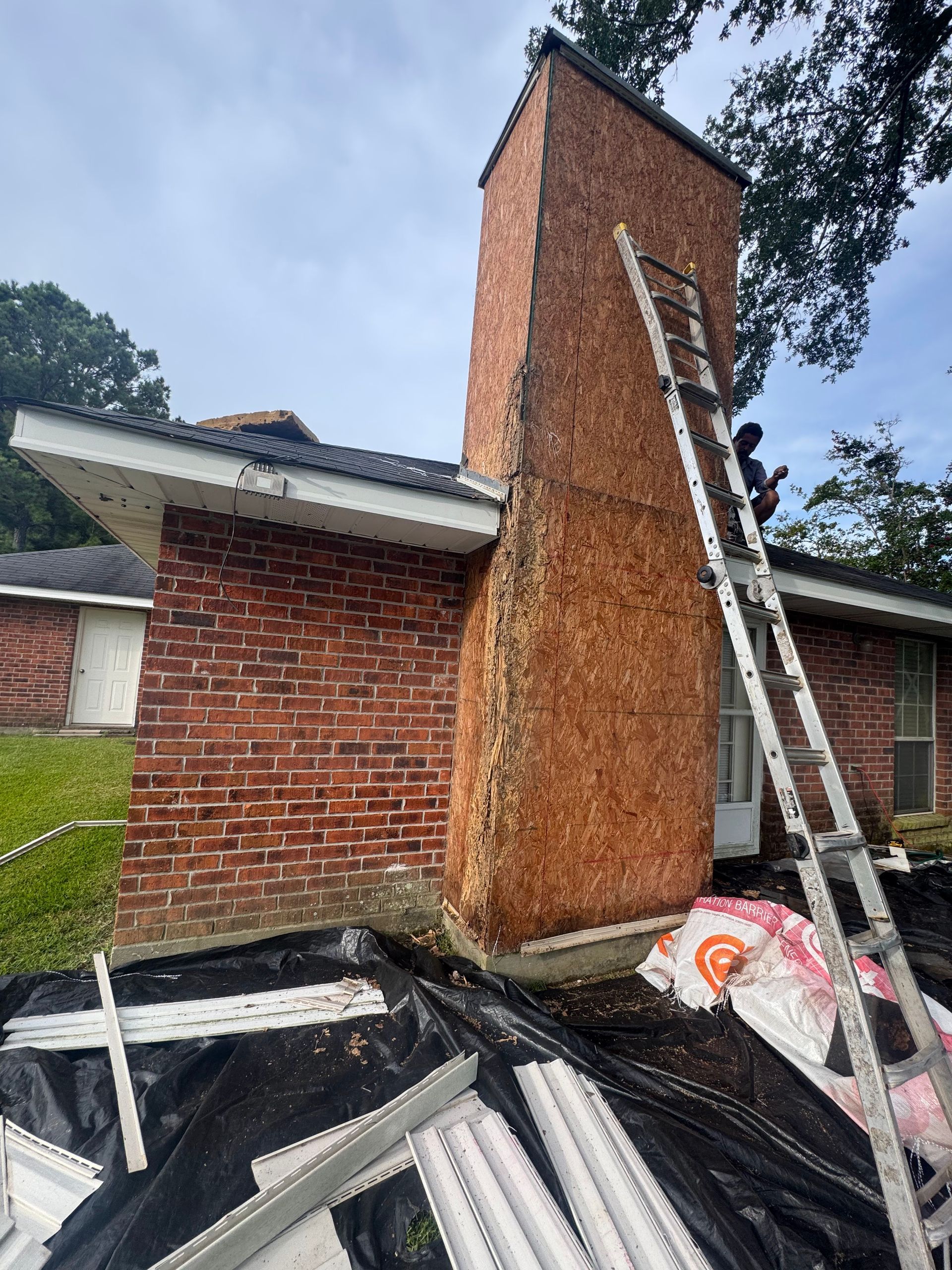 Brick chimney on a house roof with a ladder leaning against it and construction debris below