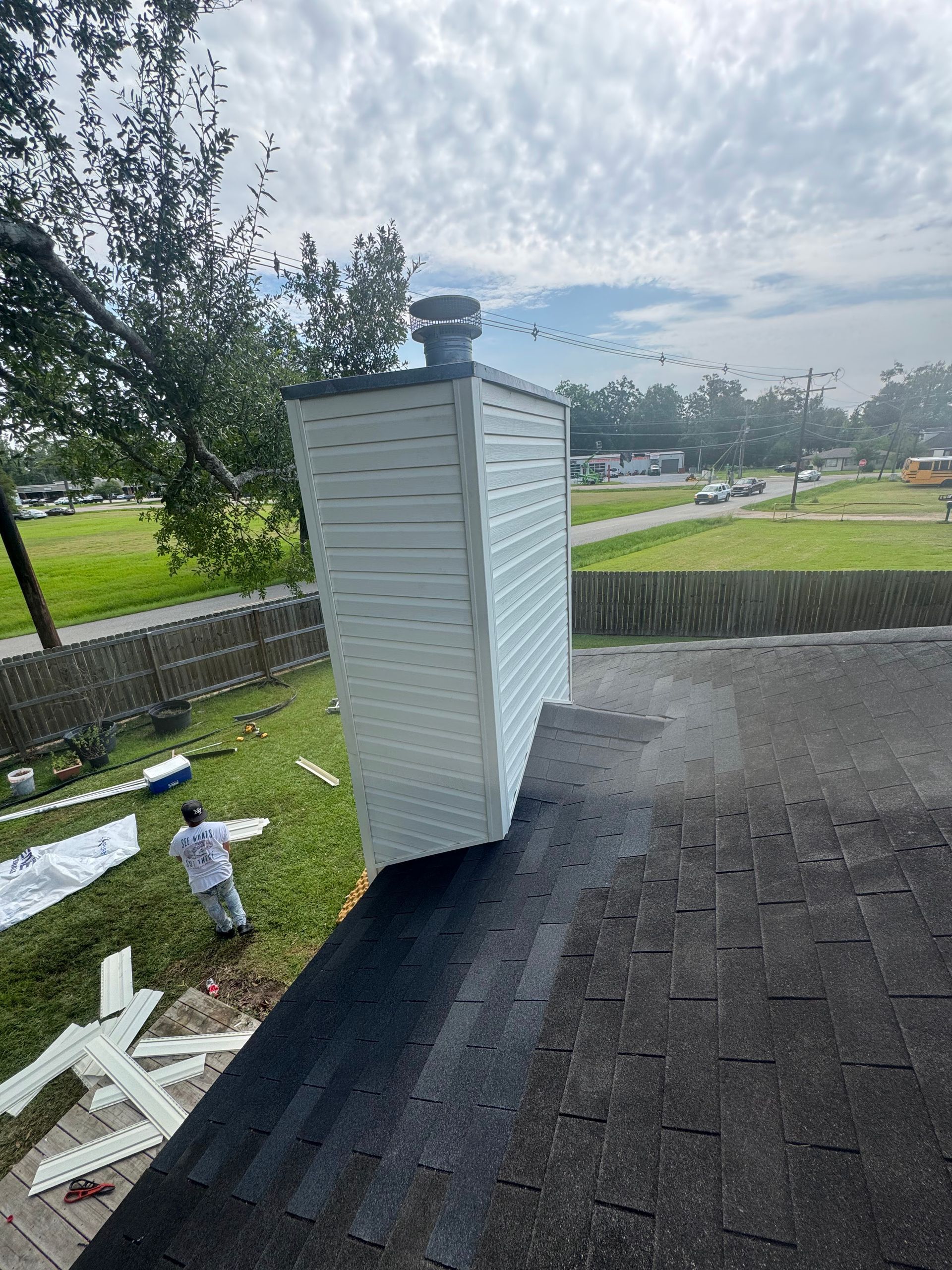 White chimney on a dark shingled roof with a backyard and trees in the background.