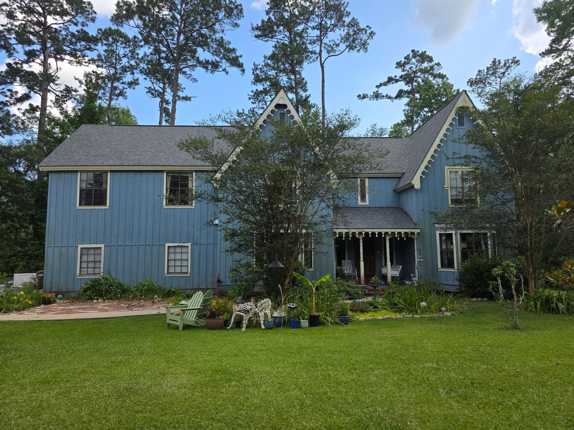 Blue two-story house with gabled roof, trees, and a large green lawn in front