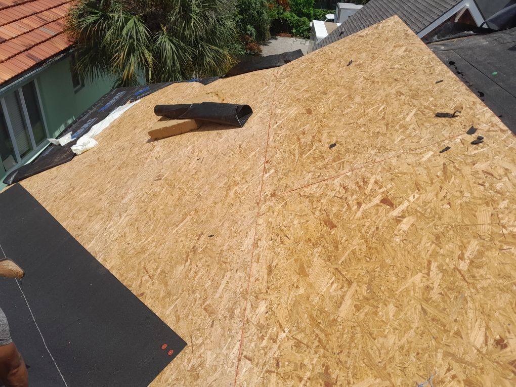 Rooftop under construction with large plywood sheathing and a loose board near the ridge.