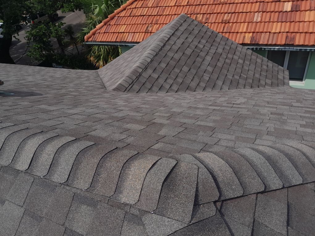 Gray shingled roof with a triangular vent and a red-tiled roof in the background