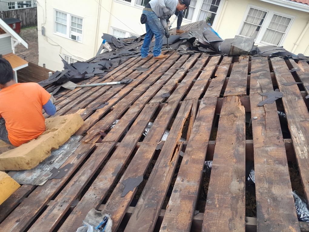 Workers repairing a roof with exposed wooden beams and tarp on a damaged house