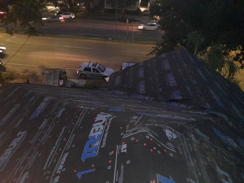 Nighttime street view from a rooftop, with a parked white pickup below and a dark, weathered roof in the foreground