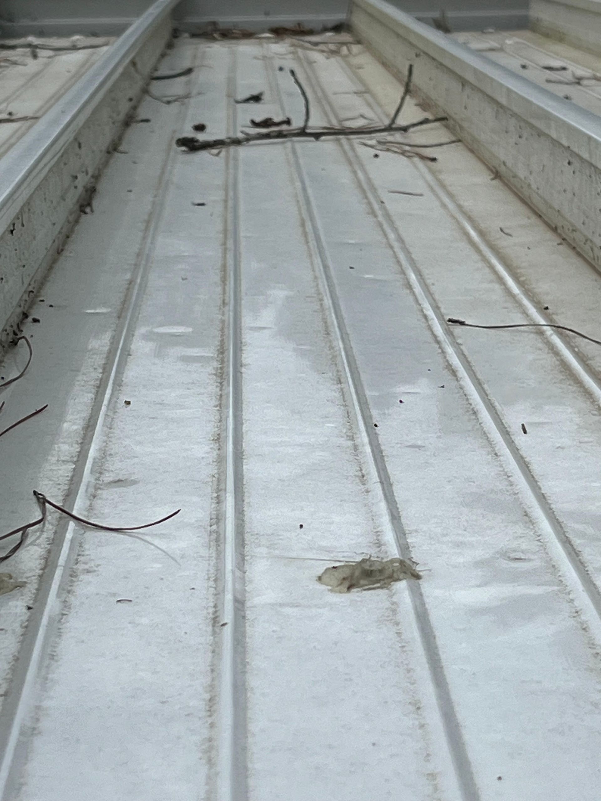 White metal roof valley with debris and leaves, viewed from the bottom looking upward