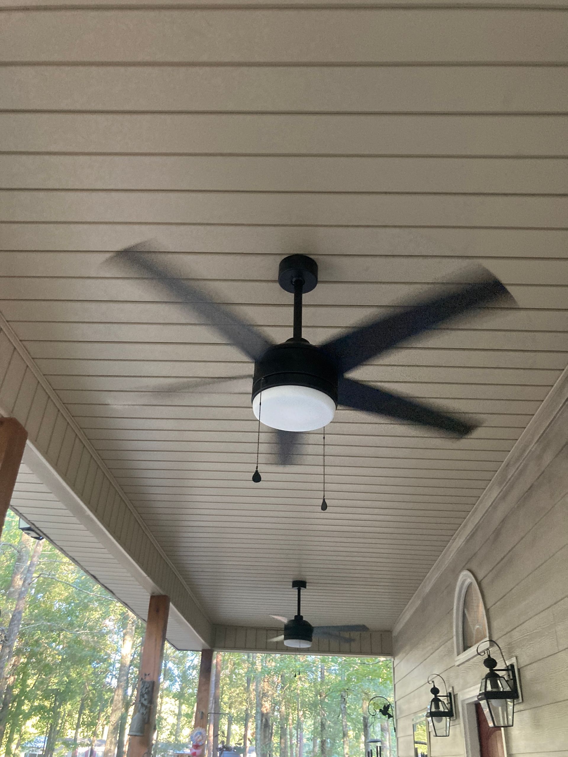 Covered porch with two black ceiling fans and beige beadboard ceiling, seen from below.