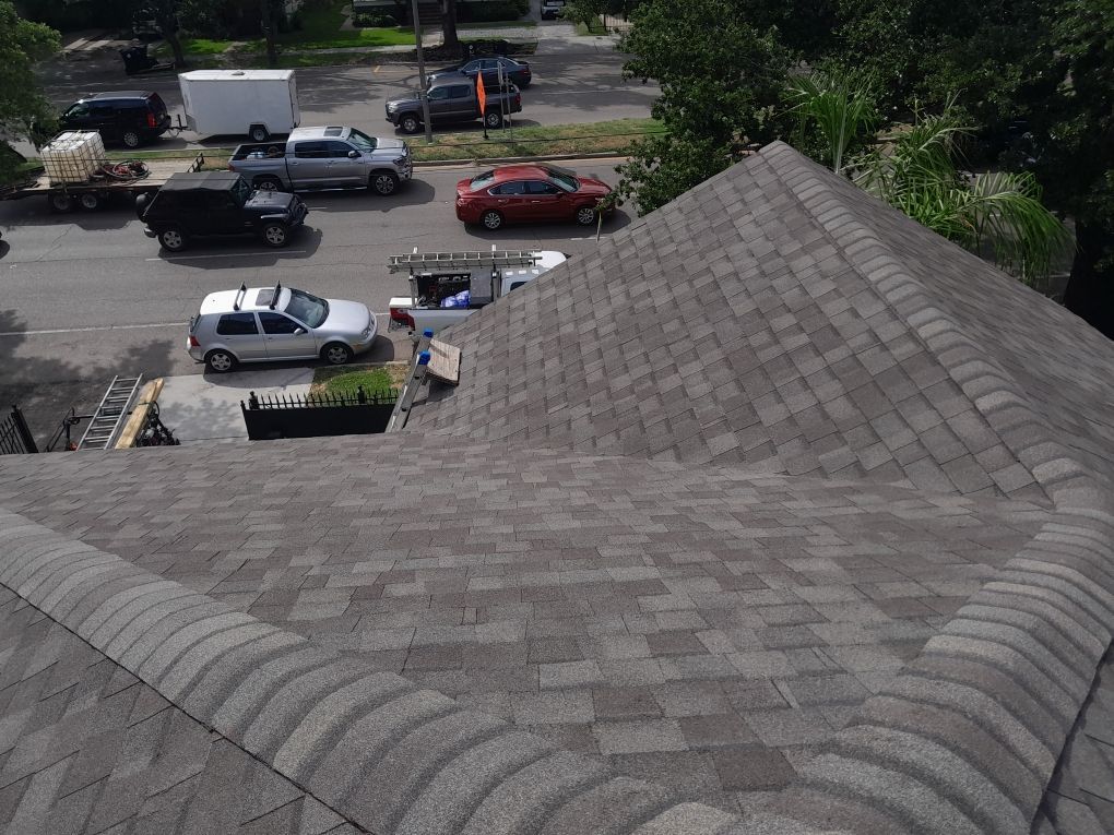 Shingled roof in foreground overlooking a parking lot with several parked cars and trees.