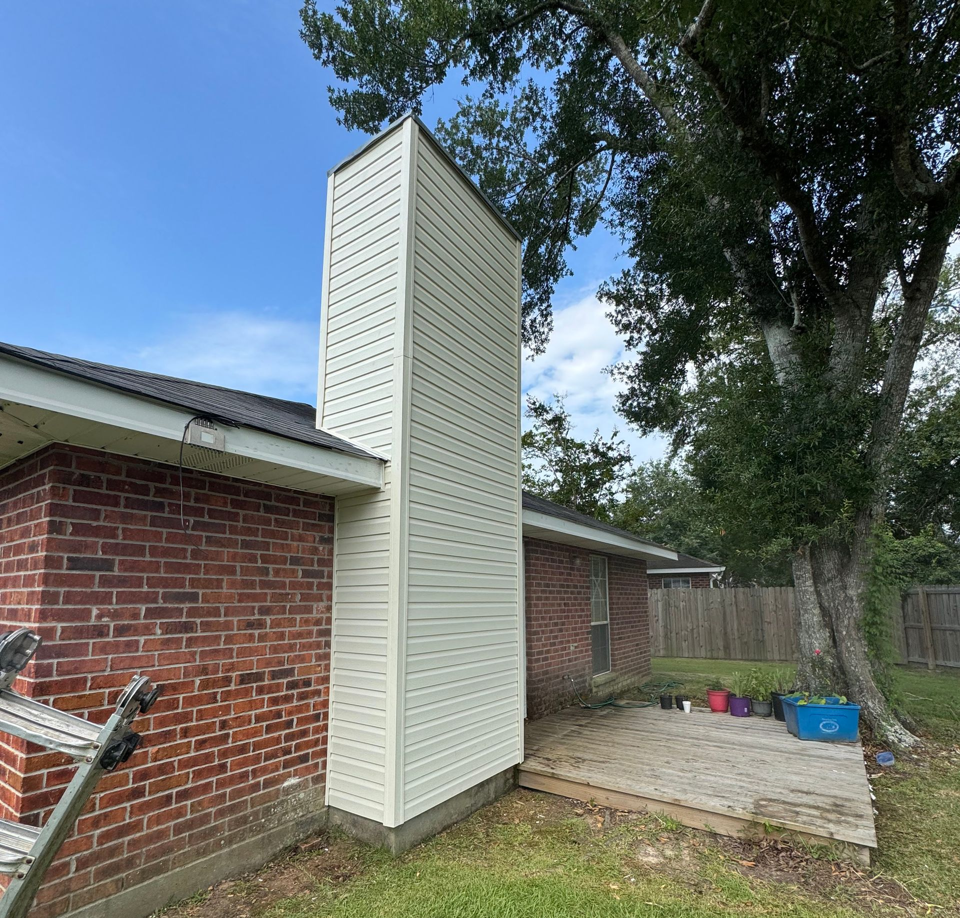 Tall white louvered utility enclosure beside a red brick house in a backyard.