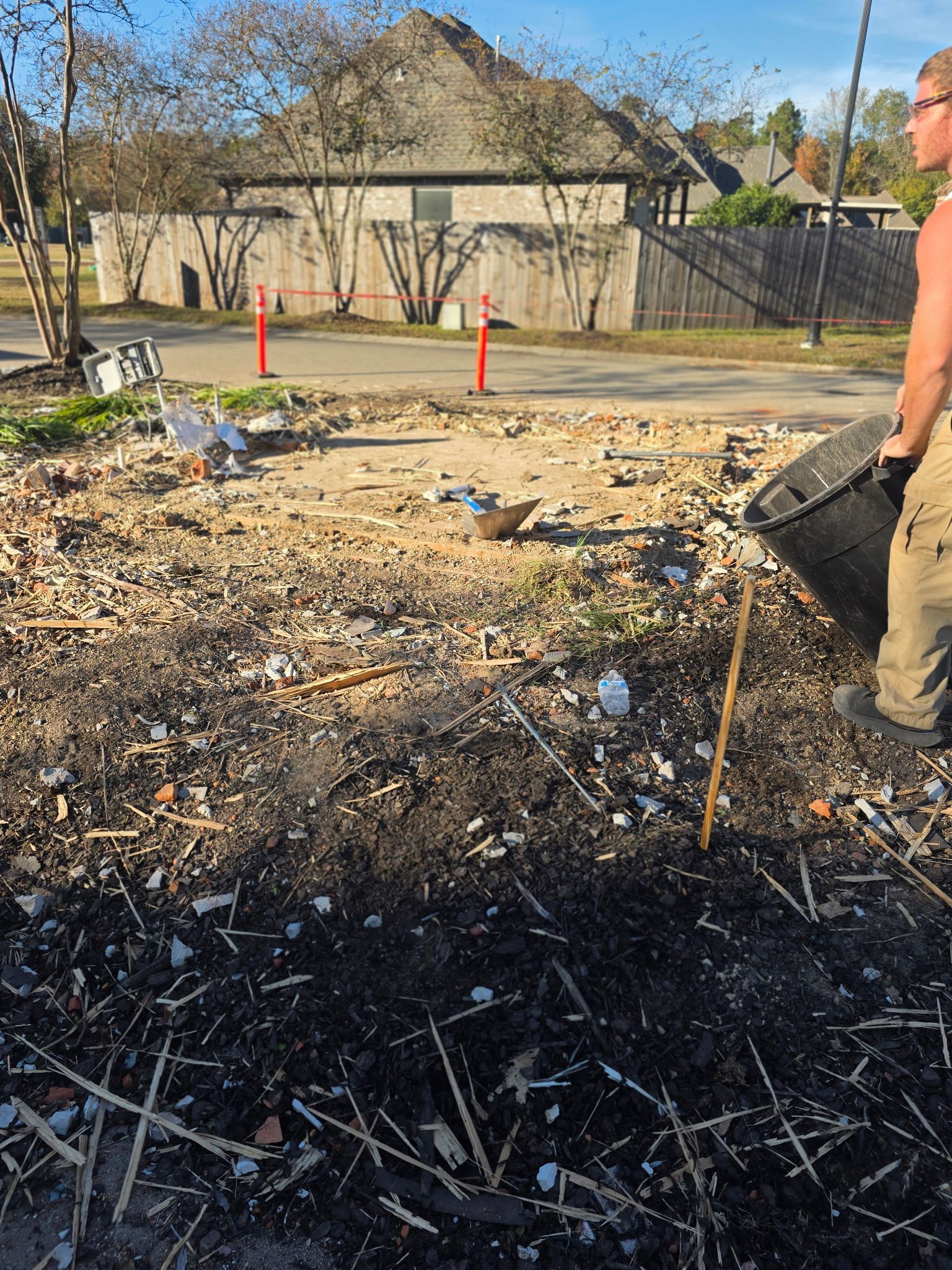 Charred debris and rubble at a construction site, with a worker in a hard hat on the right.