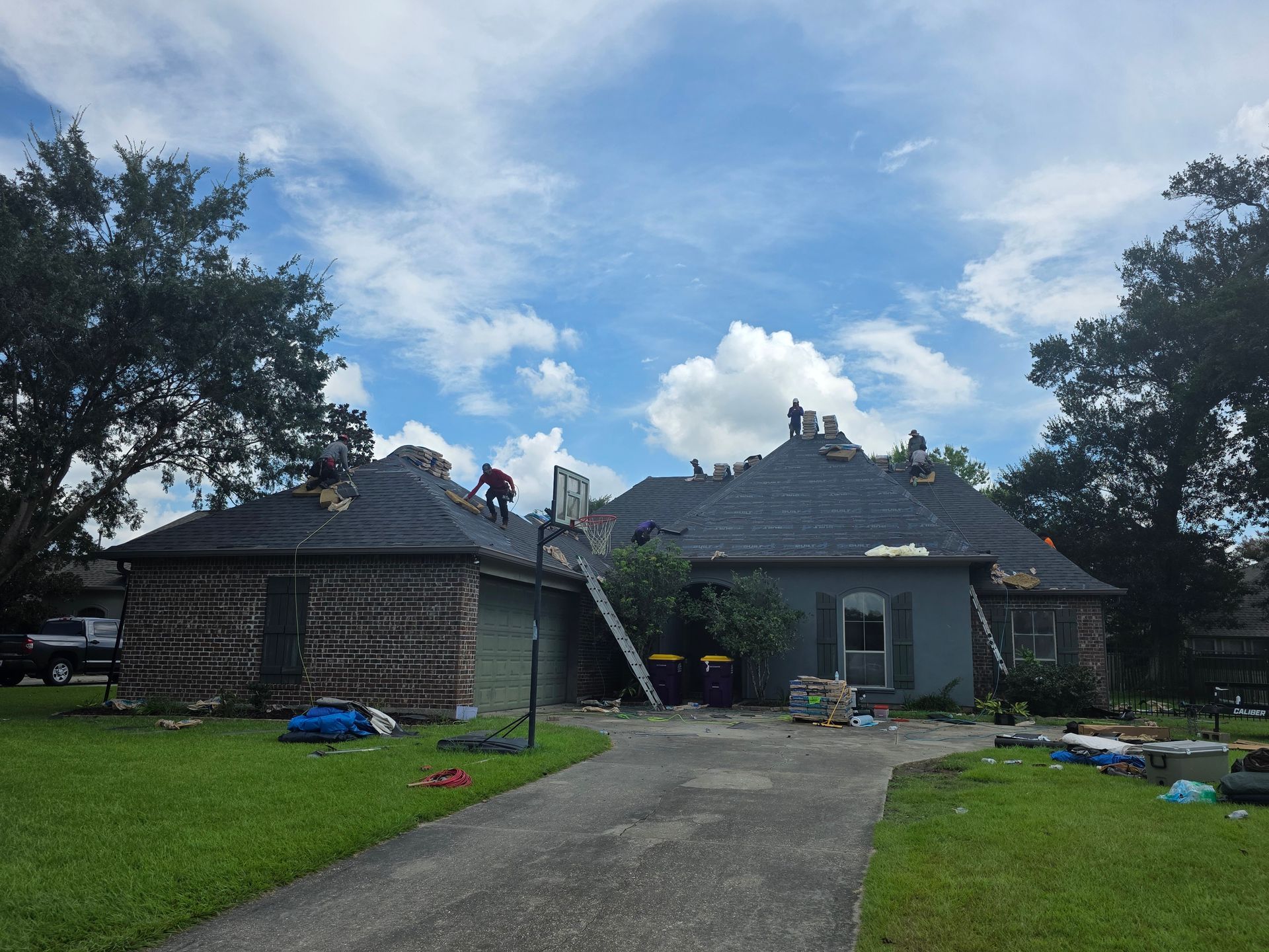 Damaged house with a ladder on the roof, scattered debris on the lawn, and a cloudy sky overhead