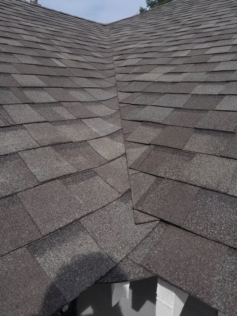 Roof shingles on a house with a damaged opening near the bottom center.