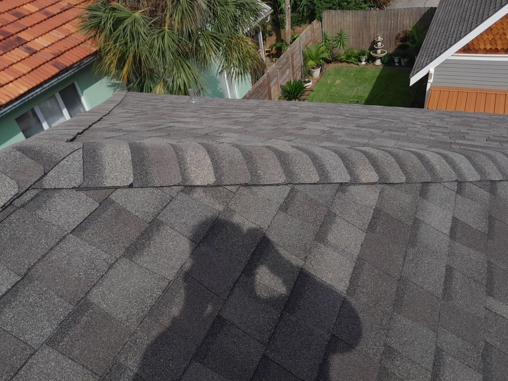 Rooftop shingles with a shadow cast across the gray roof, seen from above with houses and trees below