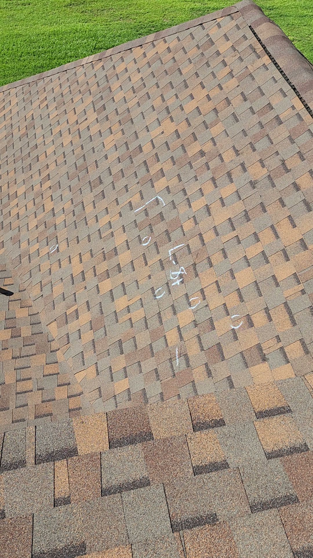 Shingled roof with brown and gray asphalt shingles beside green grass
