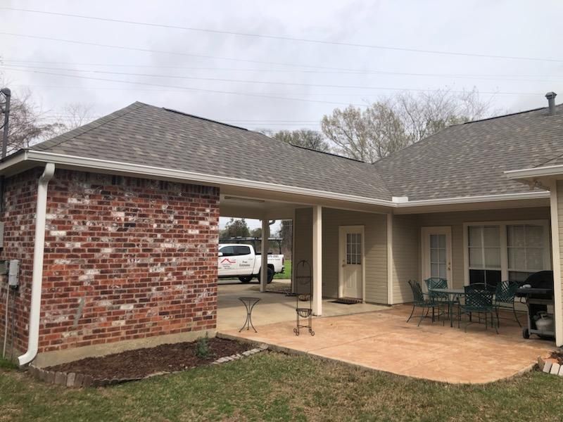 Covered brick patio with concrete floor, patio furniture, and house exterior under an overcast sky