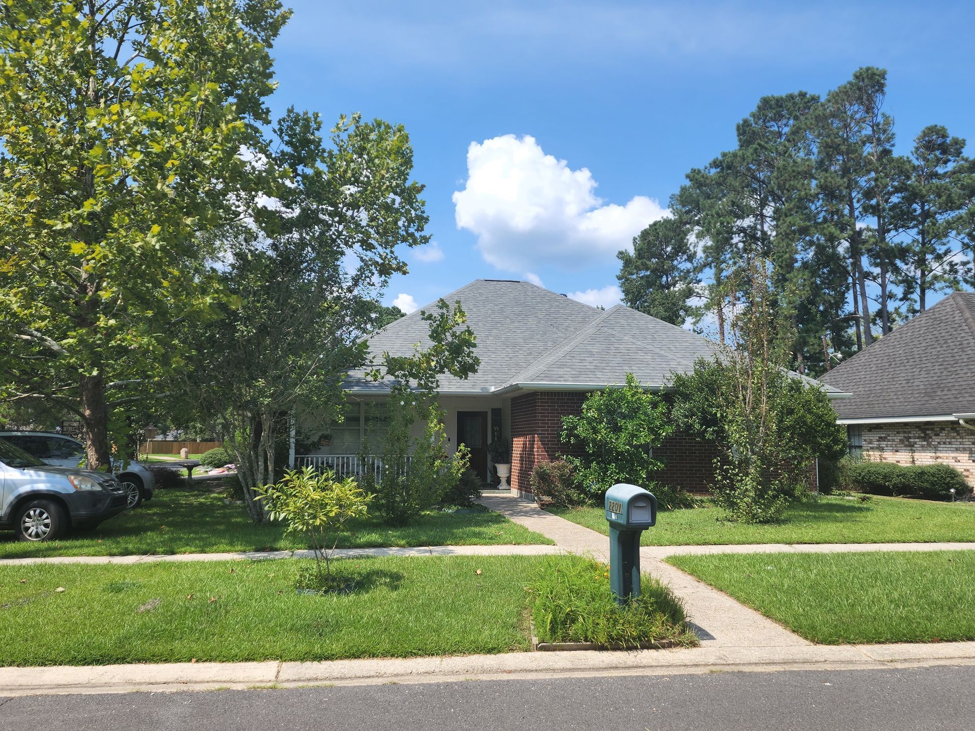 Suburban house with gray roof, green lawn, mailbox, and parked car under a blue sky.