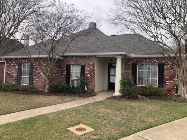 Single-story brick house with a front porch, shingled roof, and leafless trees in the yard.