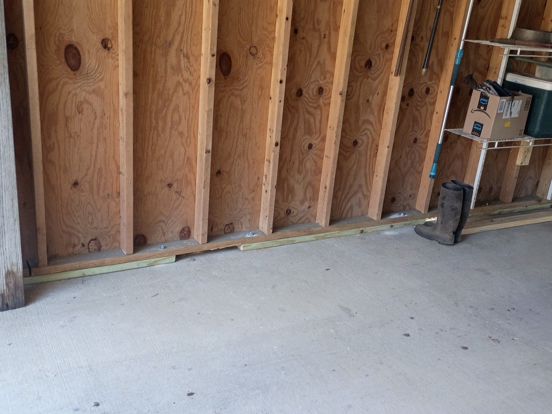 Unfinished basement with exposed wood studs, concrete floor, and storage shelves along the right wall