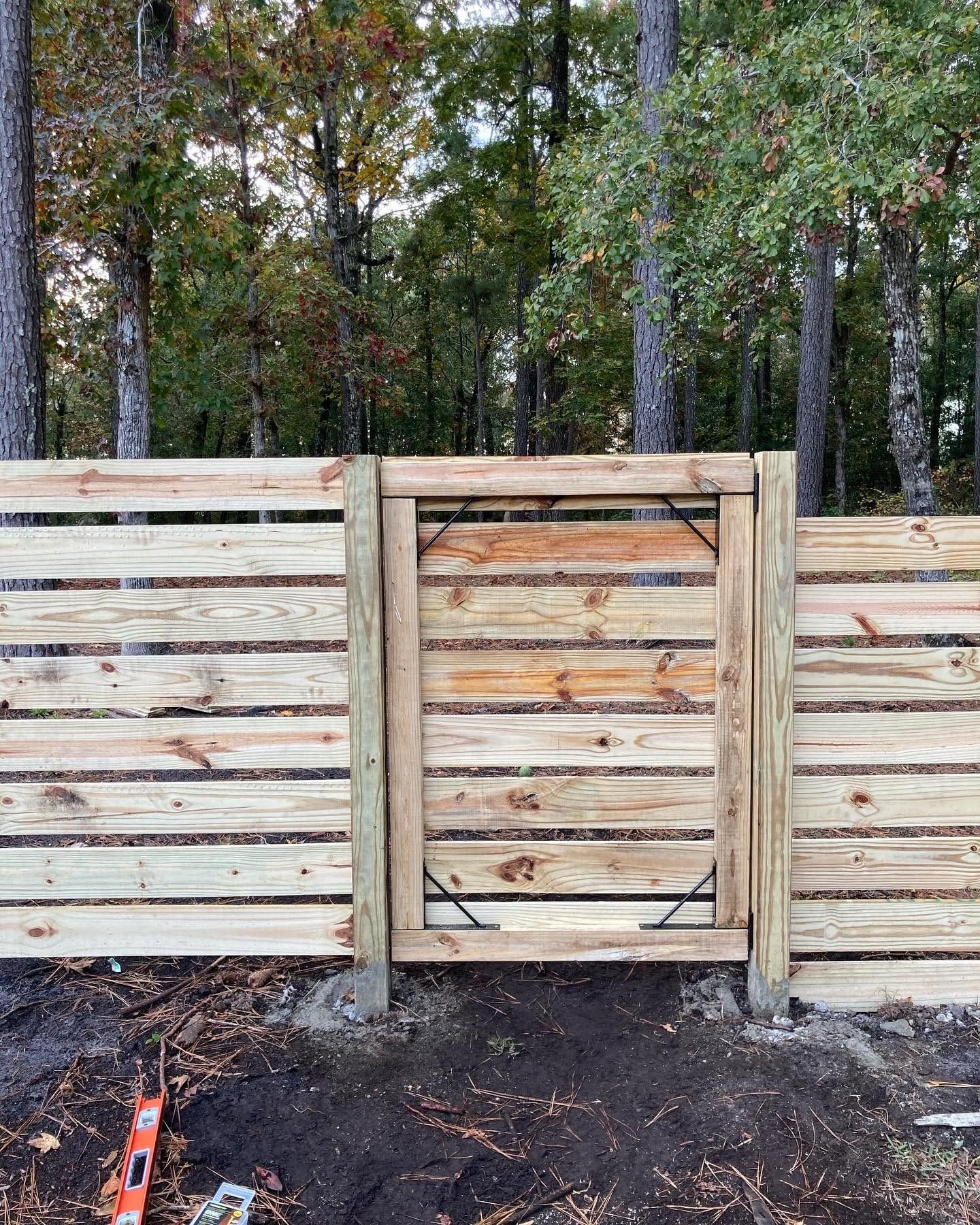 Wooden fence with a centered gate in a wooded outdoor area.