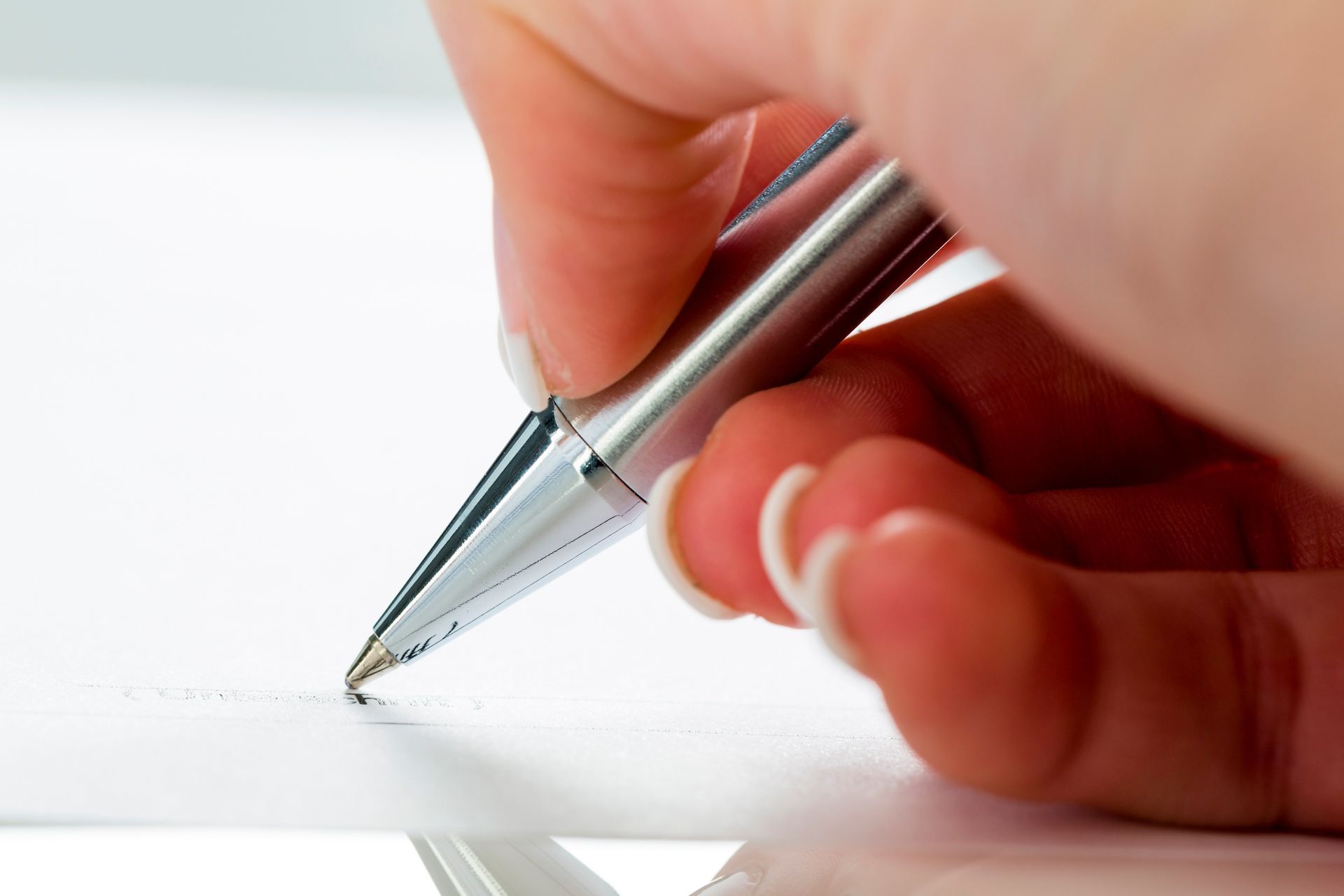 Handwriting Expert services: close-up of a hand signing with a silver pen on paper Handwriting Expert services: close-up of a hand signing with a silver pen on paper