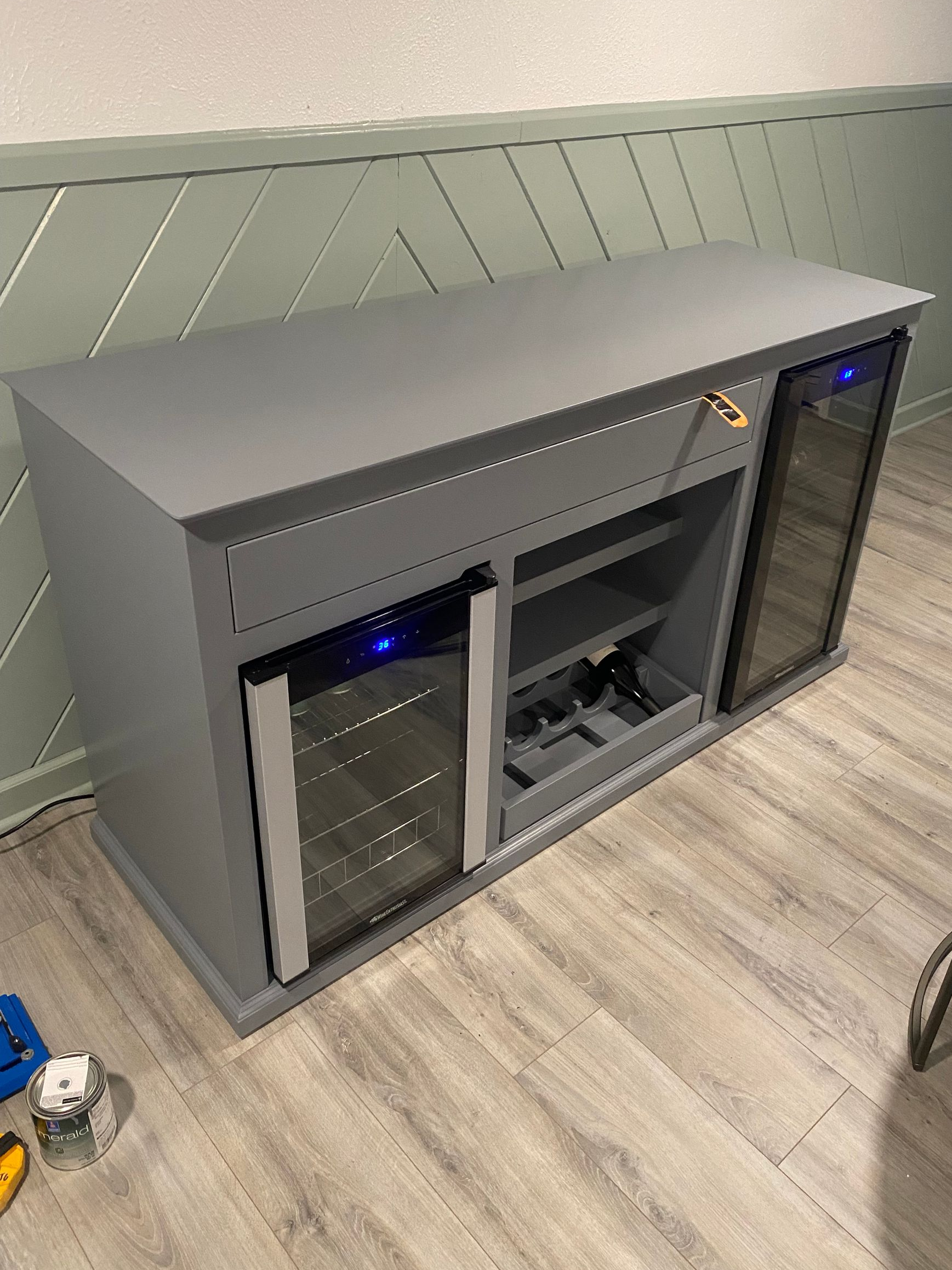 A gray cabinet with a wine cooler inside of it is sitting on a wooden floor.