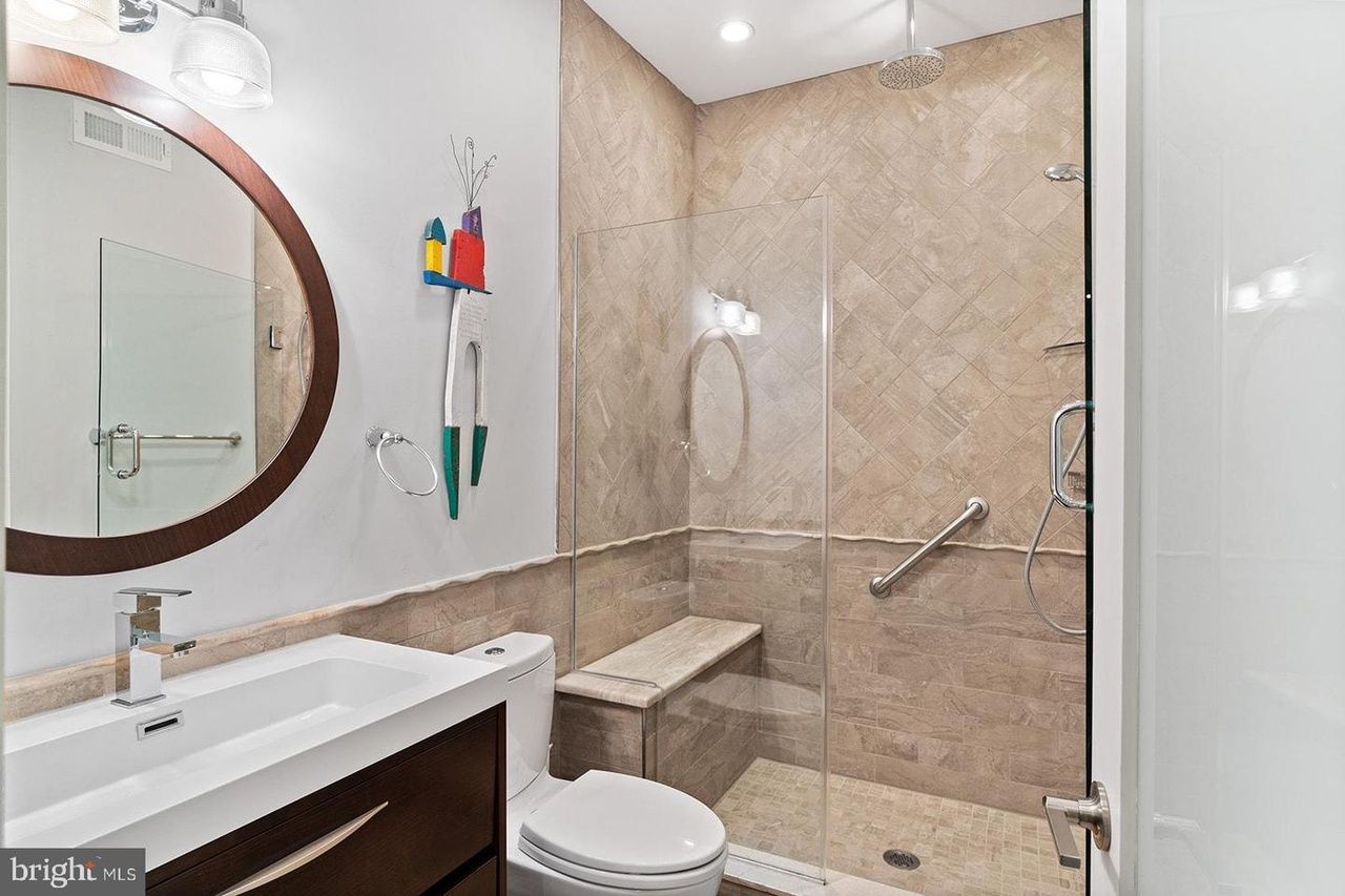 A bathroom with a toilet , sink , mirror and walk in shower.