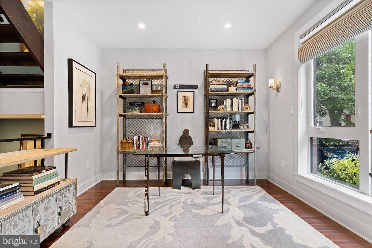 A living room with a desk and shelves and a rug