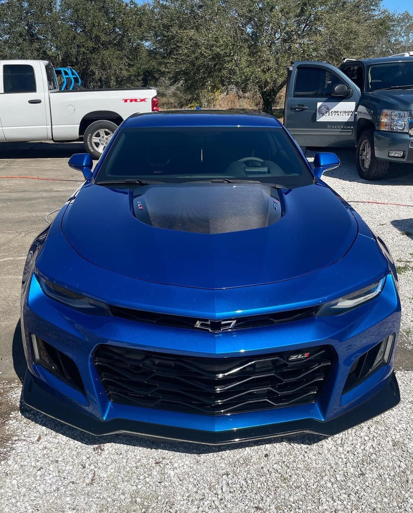 a blue car is parked in a gravel lot next to a truck .