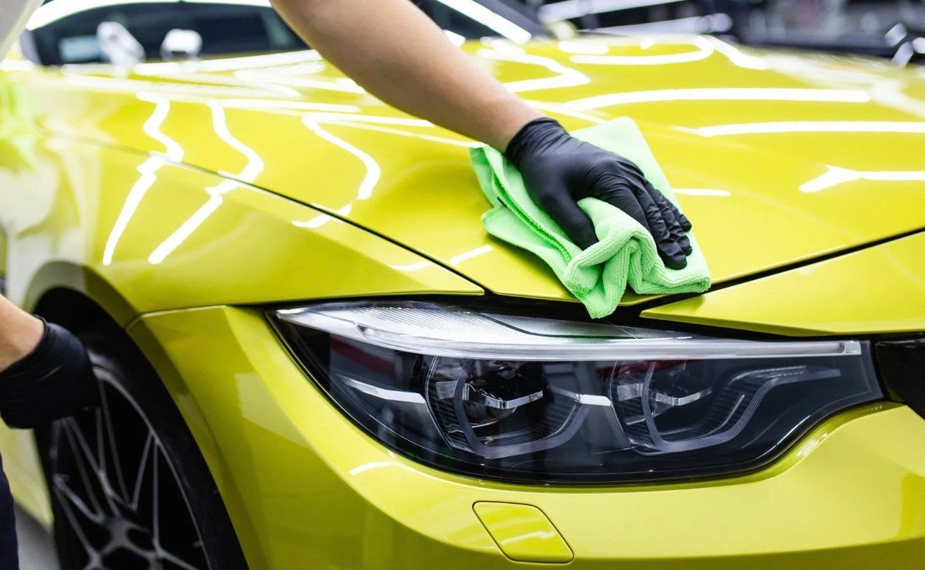 Cleaning a yellow car with a towel.