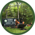 Orange skid steer parked by a black Millennium Disposal trailer in a wooded grassy area.