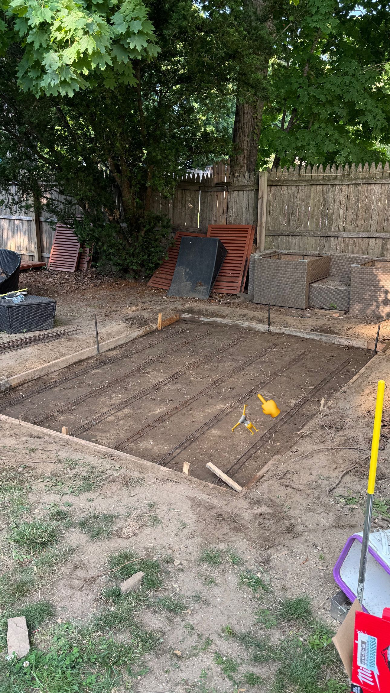 Dirt construction area beside a tree and retaining wall, with a ramp and steps leading up to a gate.