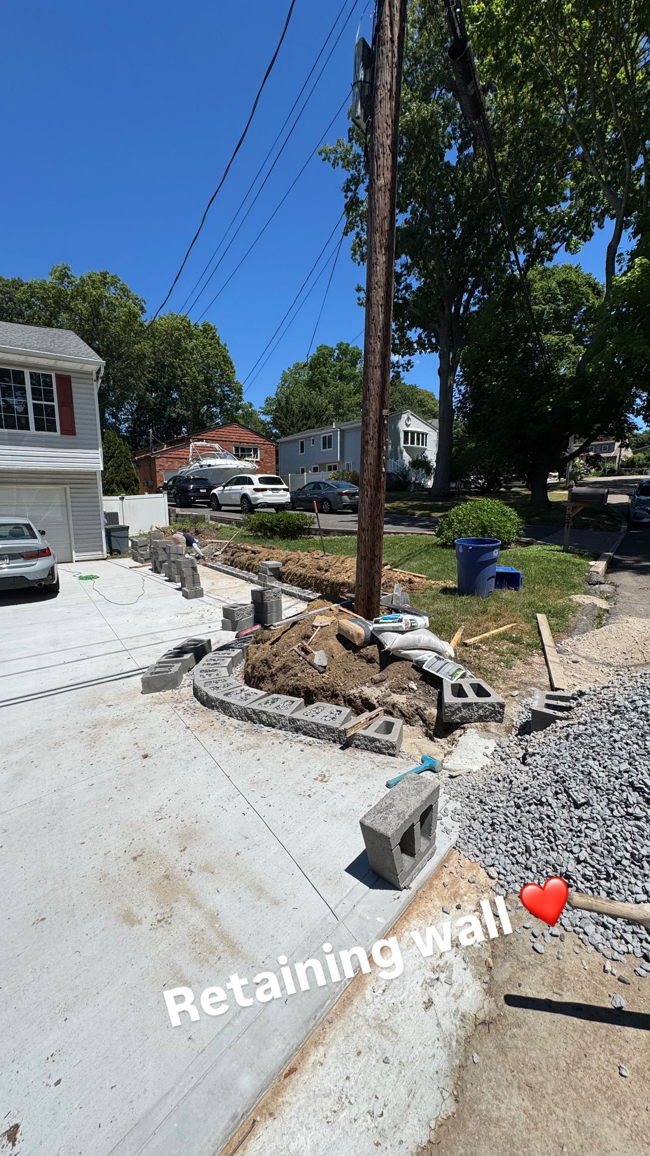 Roadside construction with a retaining wall, gravel, and utility pole under a clear blue sky