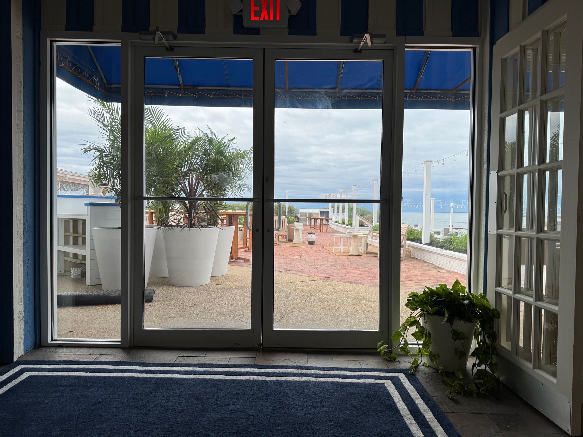 Hotel lobby entrance with glass doors, blue trim, and a view of an outdoor patio by the ocean.