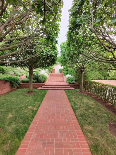 Brick path leading to red steps and a white monument framed by trees and hedges