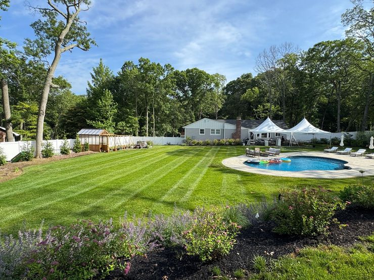 Backyard with green lawn, pool, white tents, and a house under trees on a sunny day