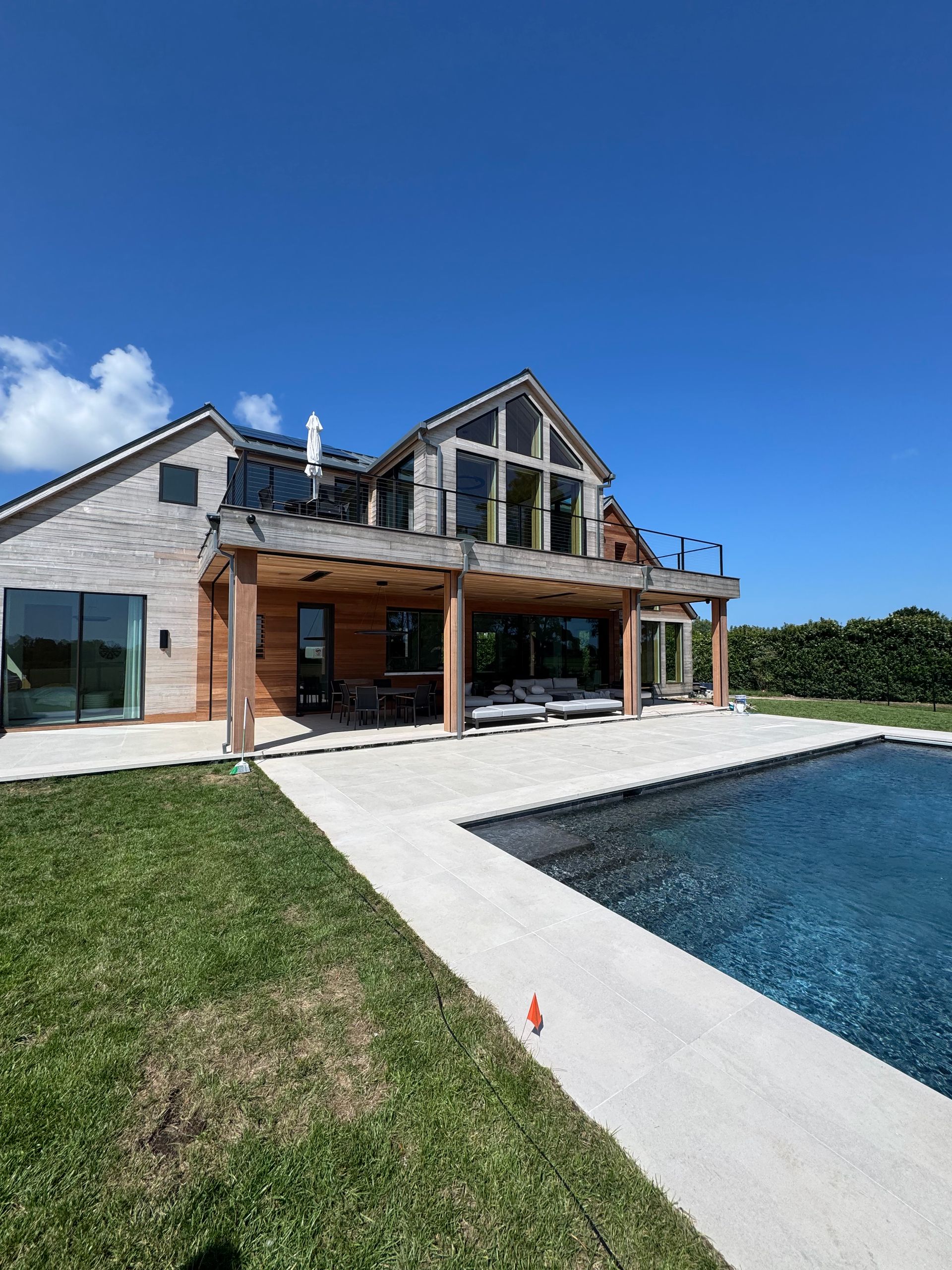 Modern house with a pool and patio beside a grassy lawn under a blue sky