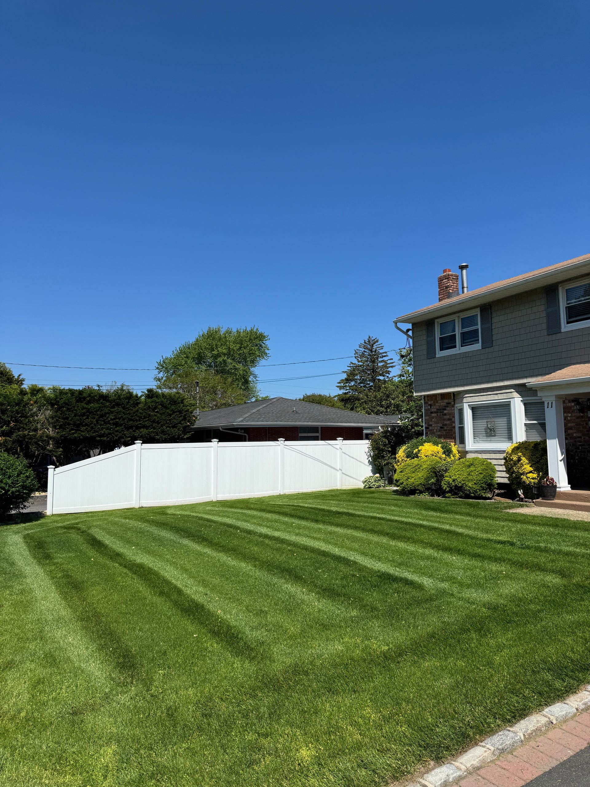 Suburban home with a white fence and striped green lawn under a clear blue sky